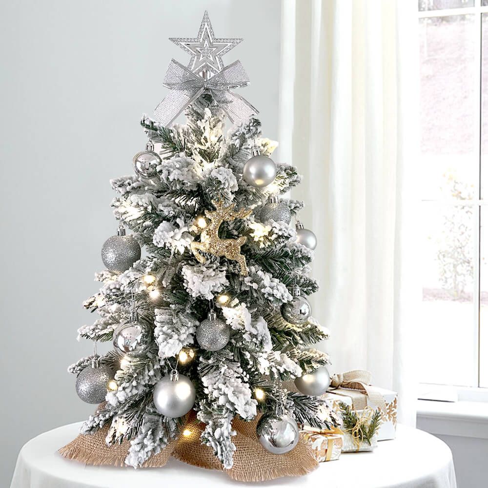 Small Xmas tree for office desk with snow-flocked branches, silver ornaments, lights, and star topper