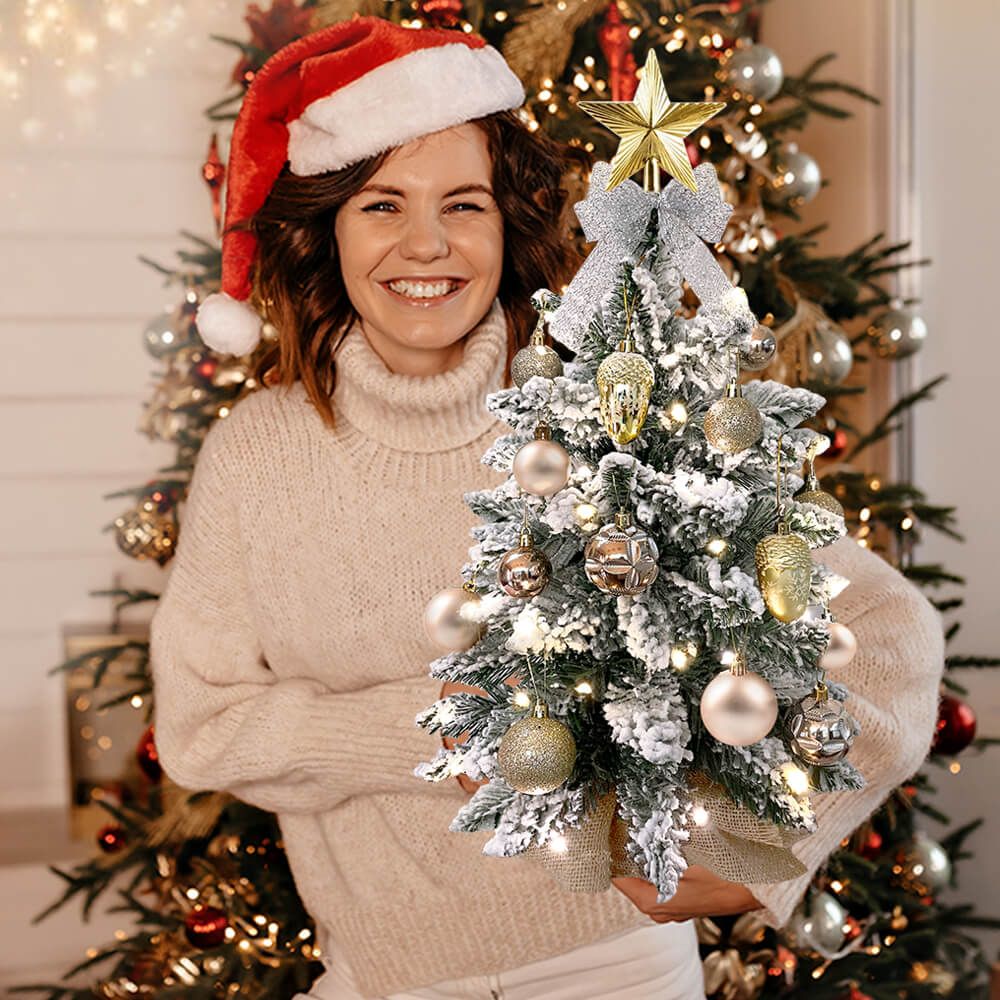 Small Xmas tree for office desk with snowy branches and gold ornaments held by woman in Santa hat