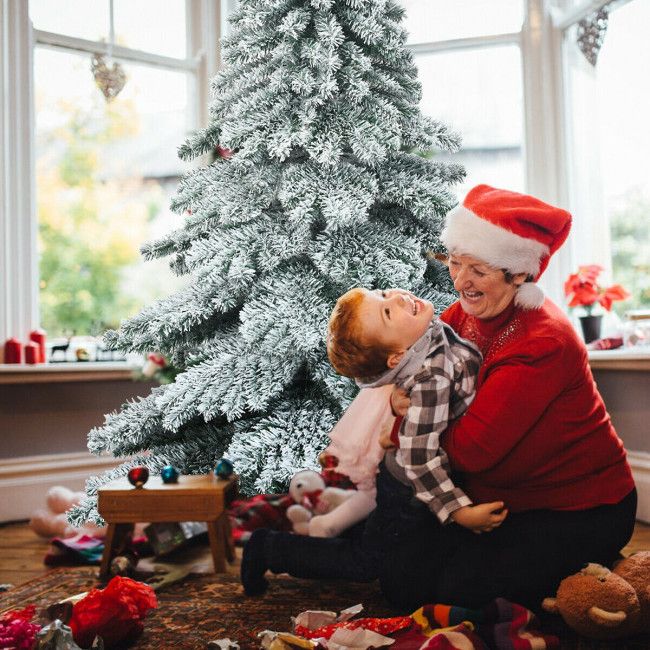 6 foot snow flocked Christmas tree with grandmother and child celebrating in cozy living room