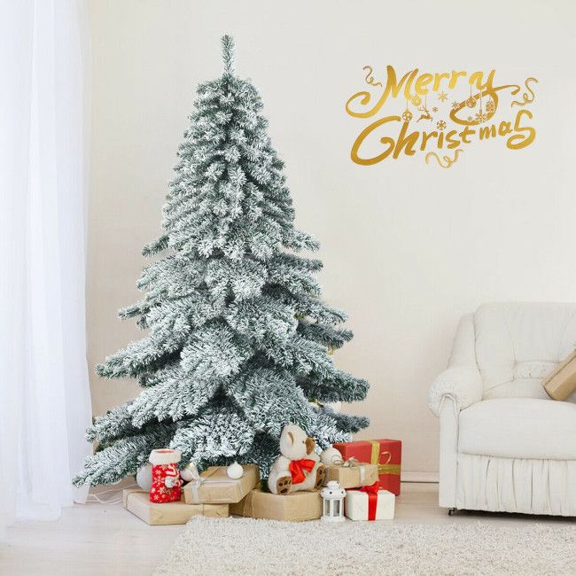 6 foot snow flocked Christmas tree decorated with gifts and teddy bear in cozy living room