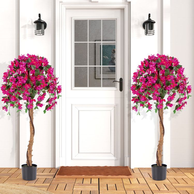 Artificial azalea tree set with vibrant pink flowers in black pots placed on wooden floor by white door