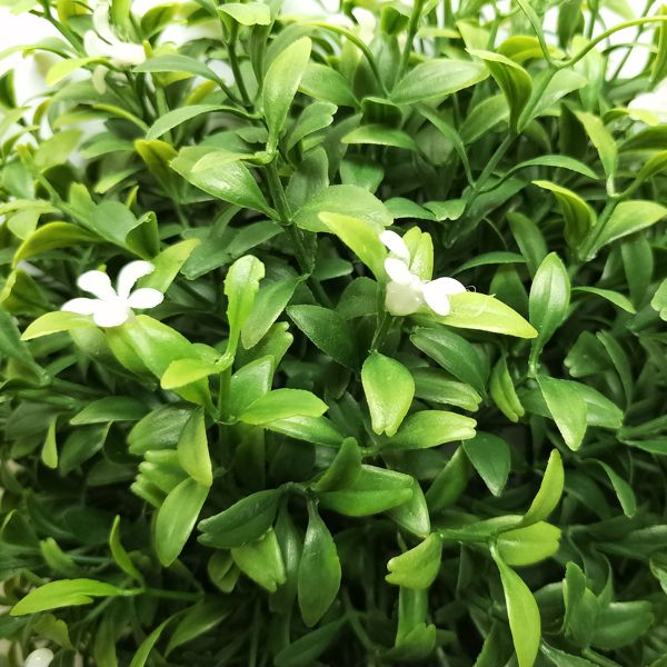Close-up of green artificial boxwood topiary ball with small white flowers and dense foliage