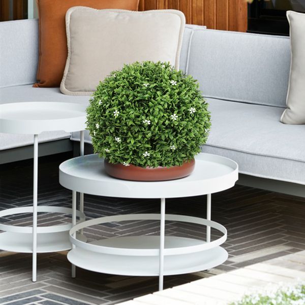 Artificial boxwood topiary ball with small white flowers on white round table in modern living room