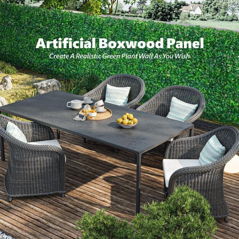 Outdoor patio with artificial boxwood wall panels creating a lush green privacy screen behind a gray dining table and wicker chairs