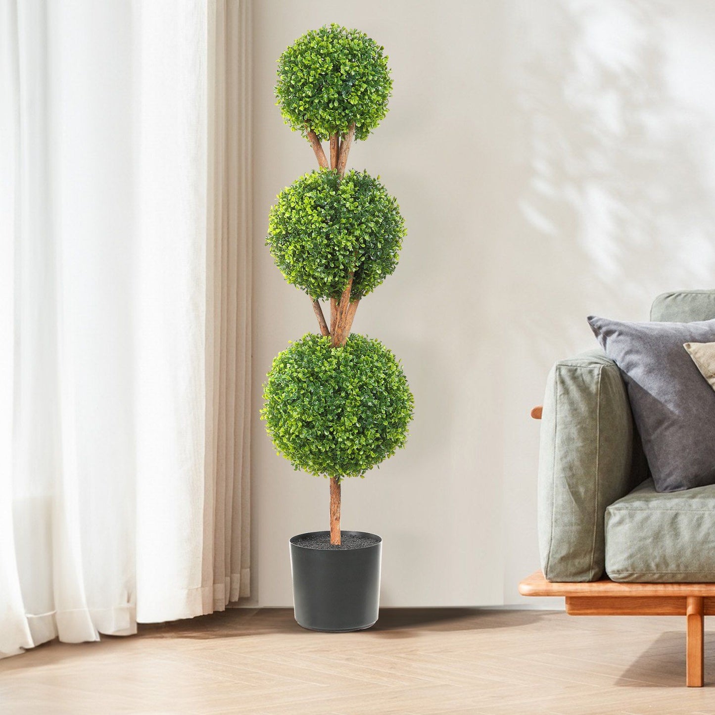 Faux boxwood trees set with three green ball-shaped topiaries in black pot by sofa