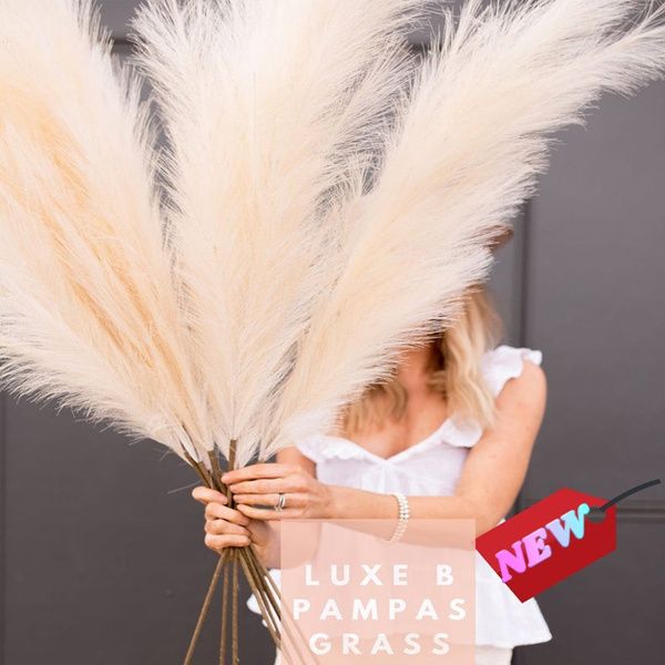 Tall artificial pampas grass decor with fluffy beige plumes held by a woman in white top