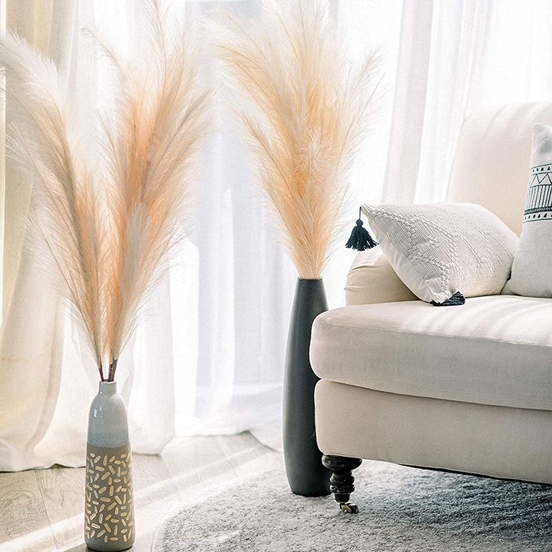 Tall artificial pampas grass decor in decorative vases next to a beige sofa in bright living room