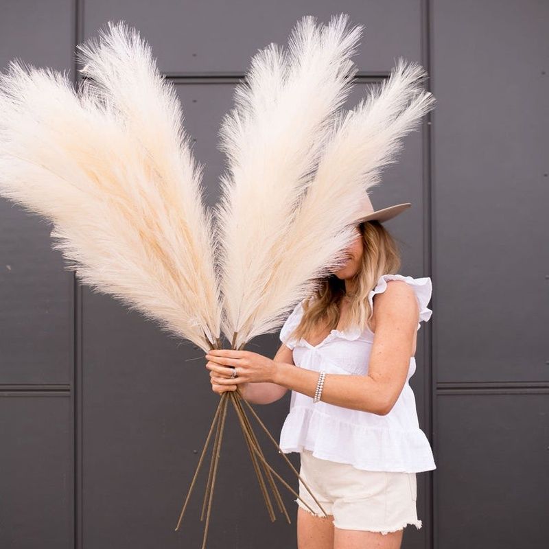Woman holding tall artificial pampas grass decor with fluffy beige plumes in casual summer outfit