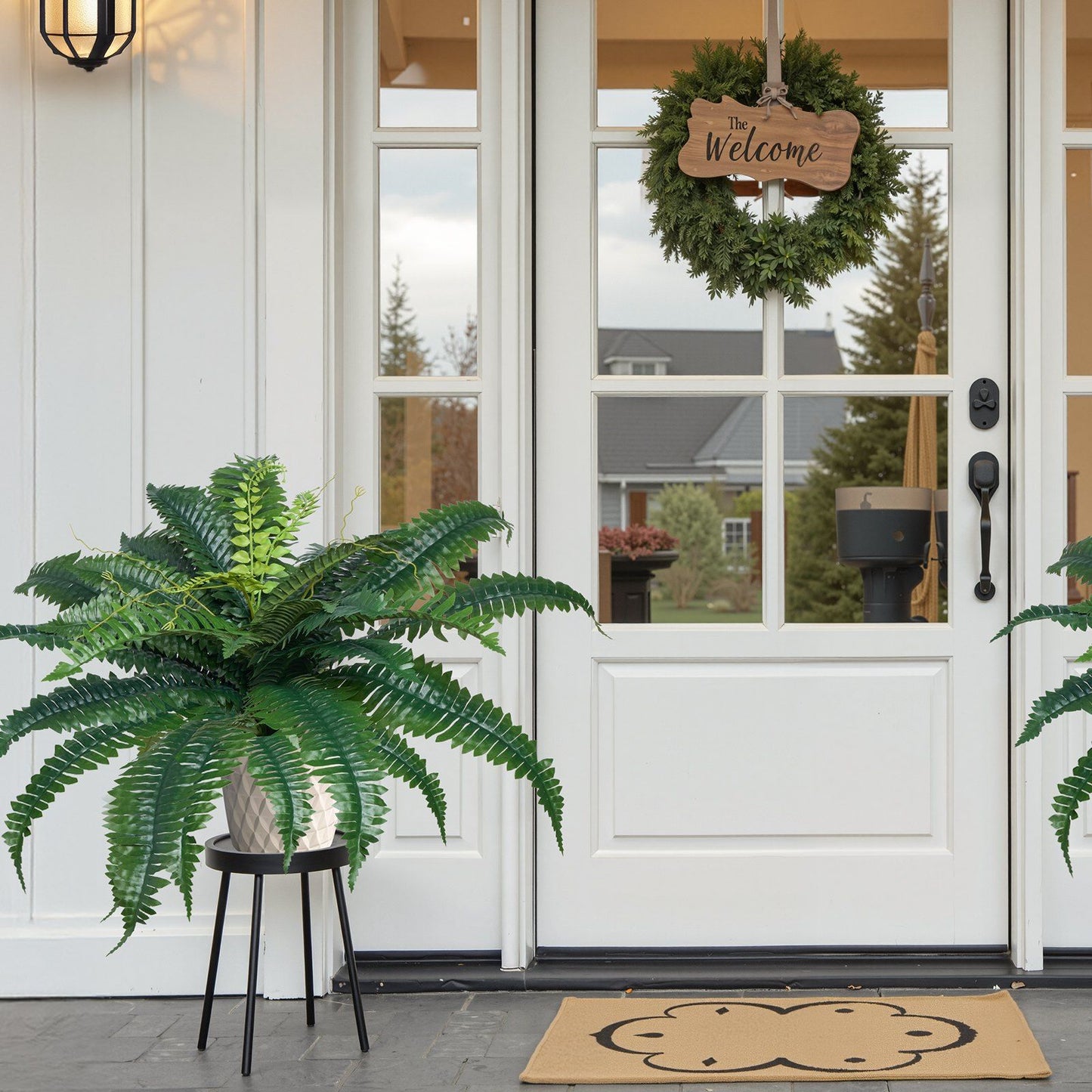 Artificial Boston ferns set displayed in grey pots on black stands near white front door with welcome wreath