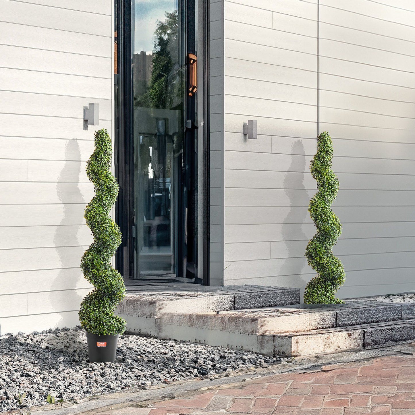 Artificial boxwood topiary tree set with spiral design in black pots placed outside modern home entrance