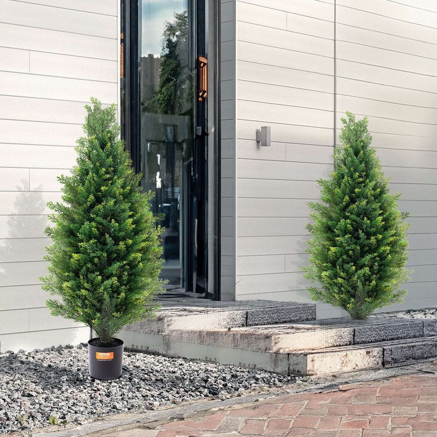 Two artificial cedar topiary trees in black pots placed outside modern house entrance
