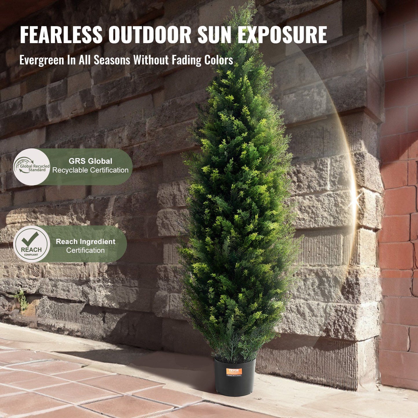 Faux cedar topiary trees in black pot standing outdoors against stone wall with evergreen foliage