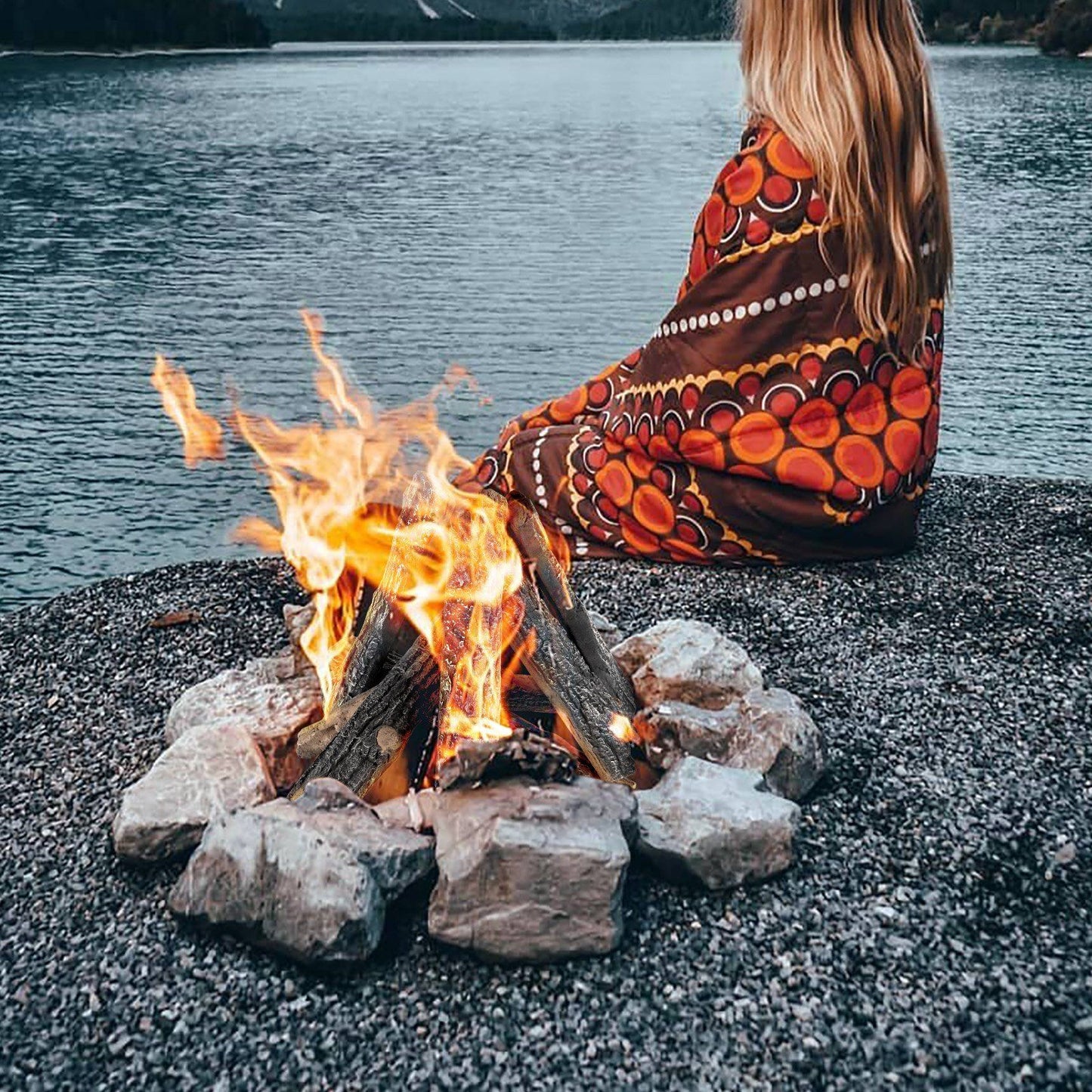 Realistic oak gas fire logs set burning with bright flames surrounded by stones near a lake