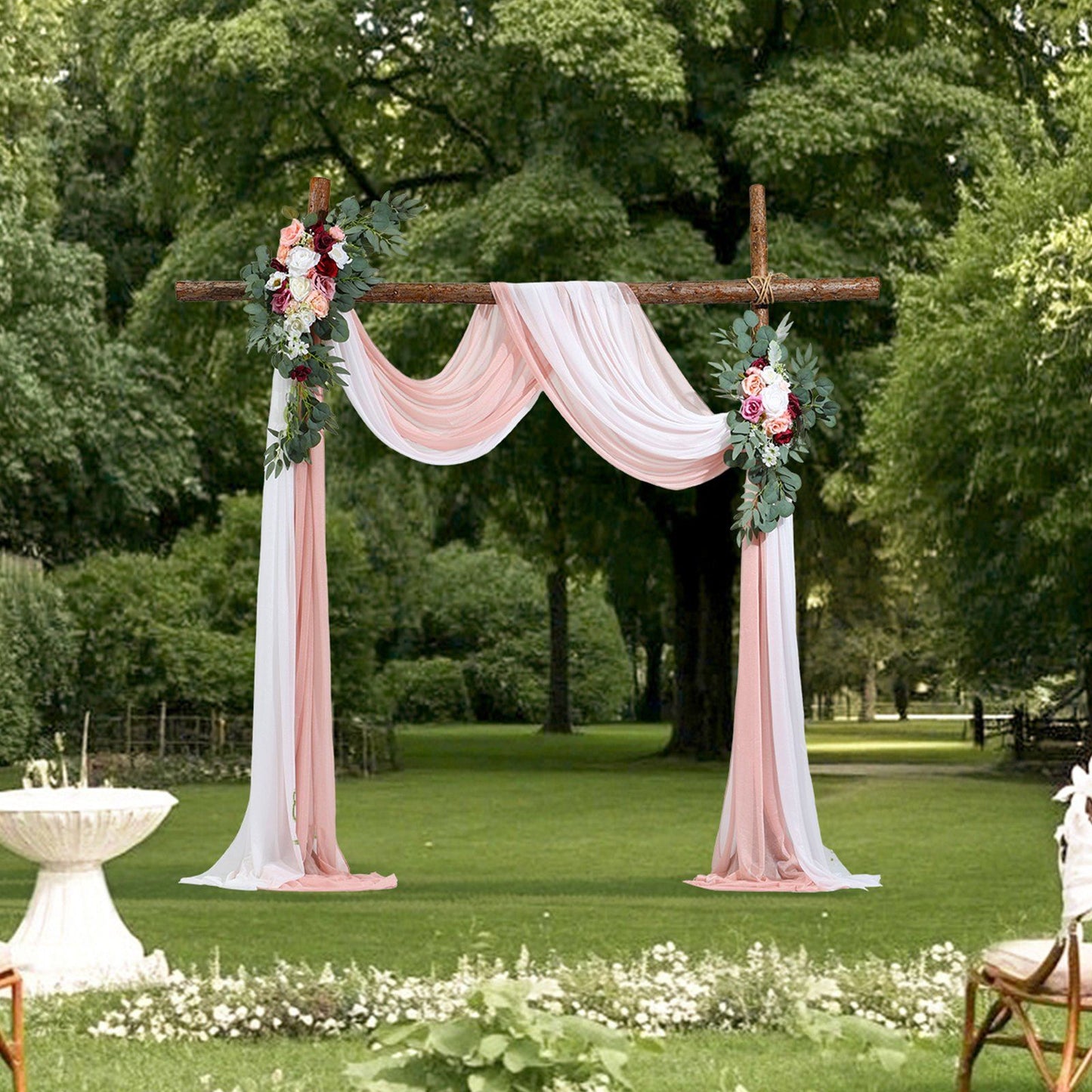 Artificial wedding arch flowers kit with pink draped fabric and floral arrangements on wooden frame in outdoor garden