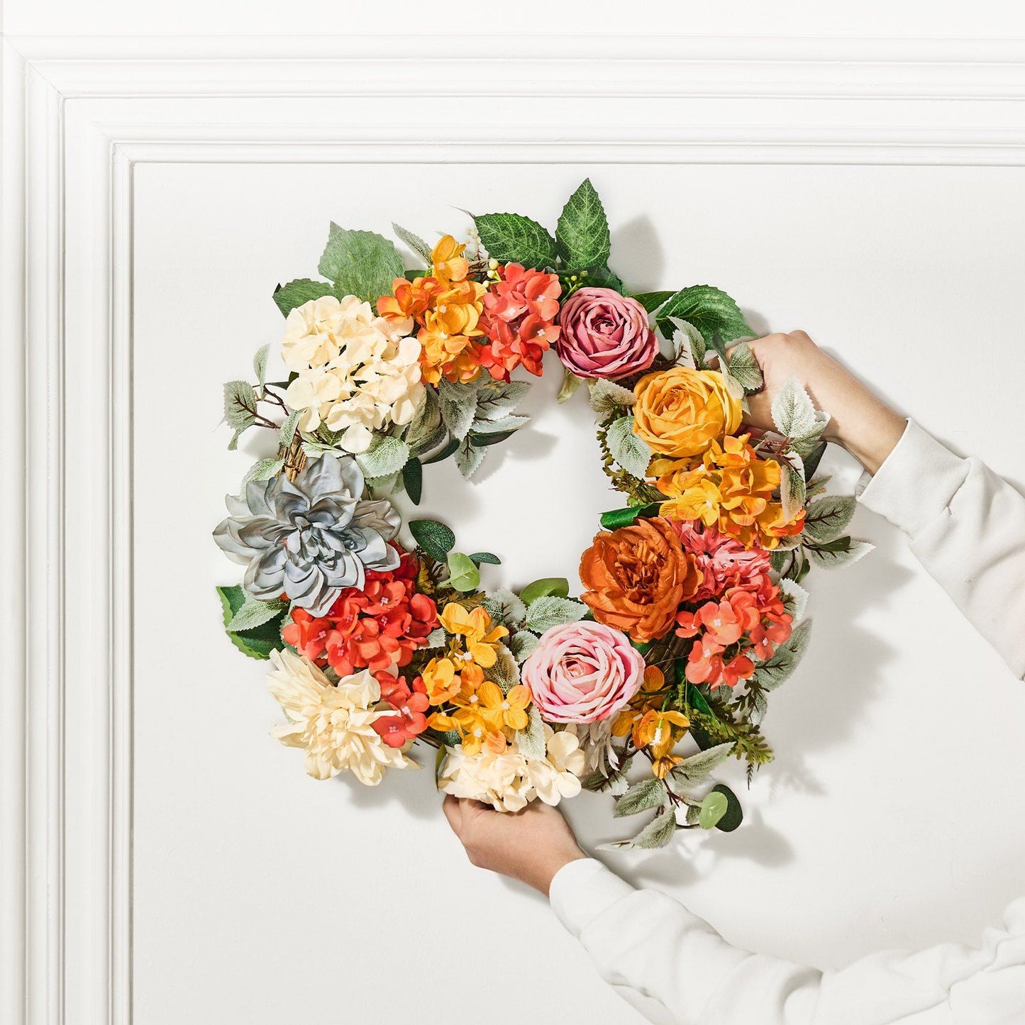 Hands holding an artificial hydrangea rose wreath with colorful flowers and green leaves