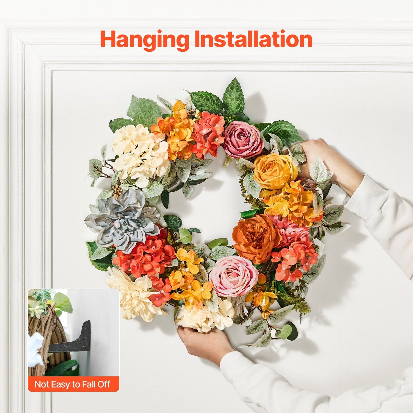Artificial hydrangea rose wreath in vibrant fall colors being hung on white wall for decoration