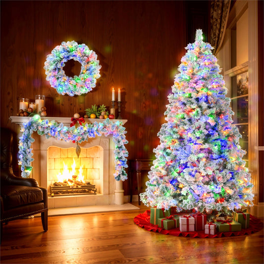 6ft snow flocked Christmas tree set with colorful lights and presents next to a decorated fireplace
