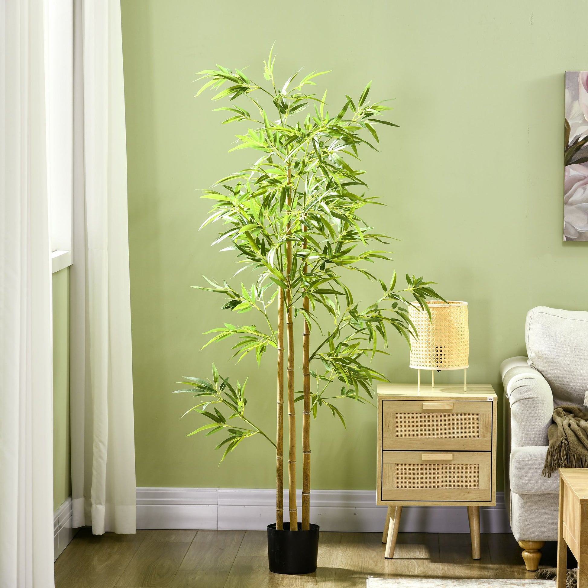 Artificial bamboo tree 6ft tall with green leaves in a black pot next to a wooden nightstand and couch