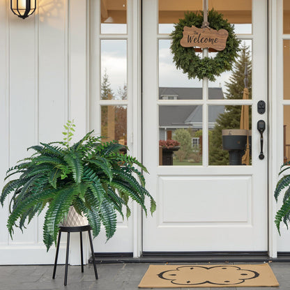 Artificial Boston fern plant in white pot on black stand placed near white front door with welcome wreath