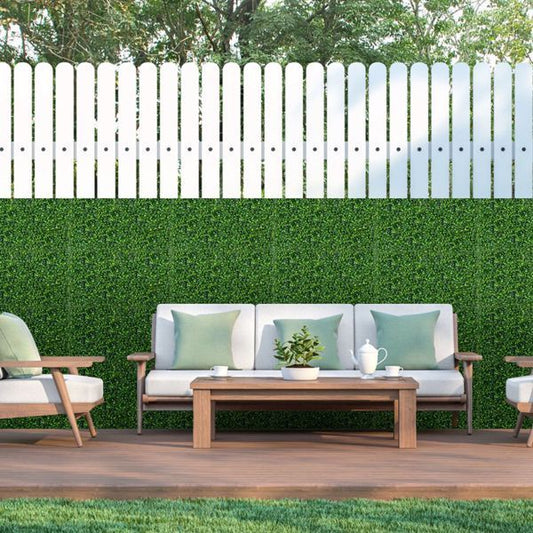Artificial boxwood hedge panels creating a lush green privacy wall behind outdoor seating area