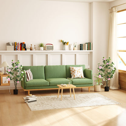 Living room with green sofa and artificial camellia flowers in pots on either side near windows
