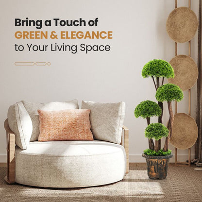 Artificial cedar topiary tree with layered green foliage in a decorative pot beside a beige modern chair