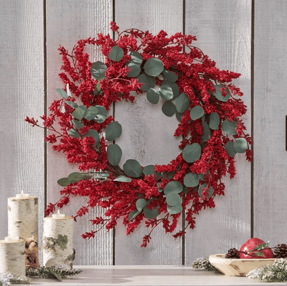 Artificial Christmas wreath with eucalyptus and red berries hanging on white wooden wall