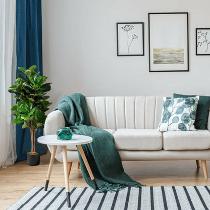 Stylish living room featuring an artificial fiddle leaf fig tree next to a modern sofa and decorative artwork