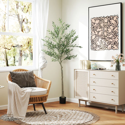 Artificial olive tree indoor in black pot next to wicker chair and white cabinet in bright living room