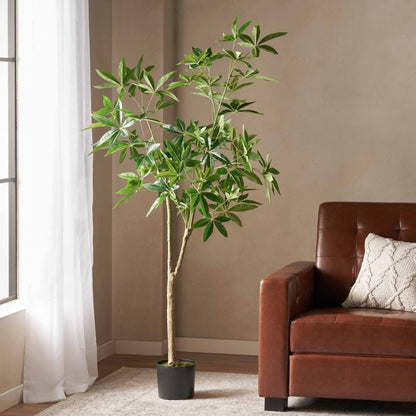Tall artificial pachira money tree with green leaves in black pot beside brown leather sofa