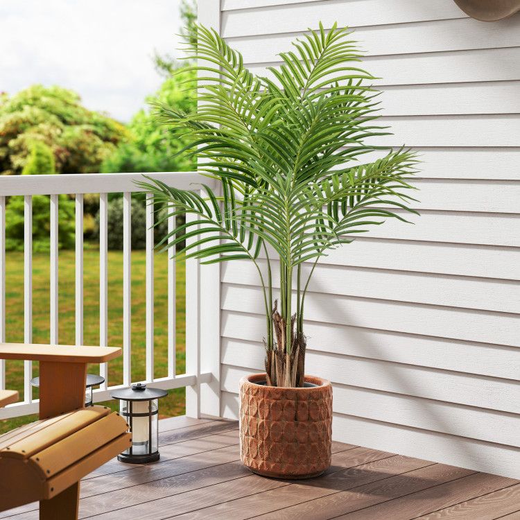 Artificial palm trees for home decor in a textured planter on a wooden porch next to a chair and lantern