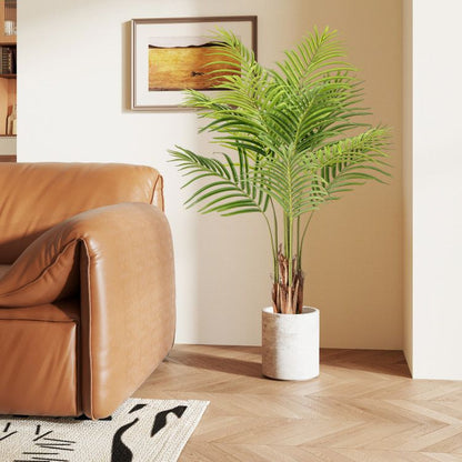 Artificial palm trees for home decor in a white pot next to a brown leather sofa in a modern living room