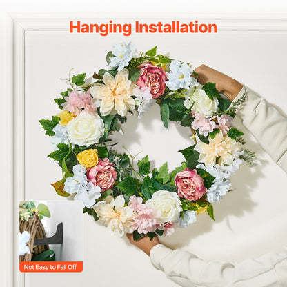 Hands hanging artificial peony hydrangea wreath with mixed flowers and green leaves on white wall