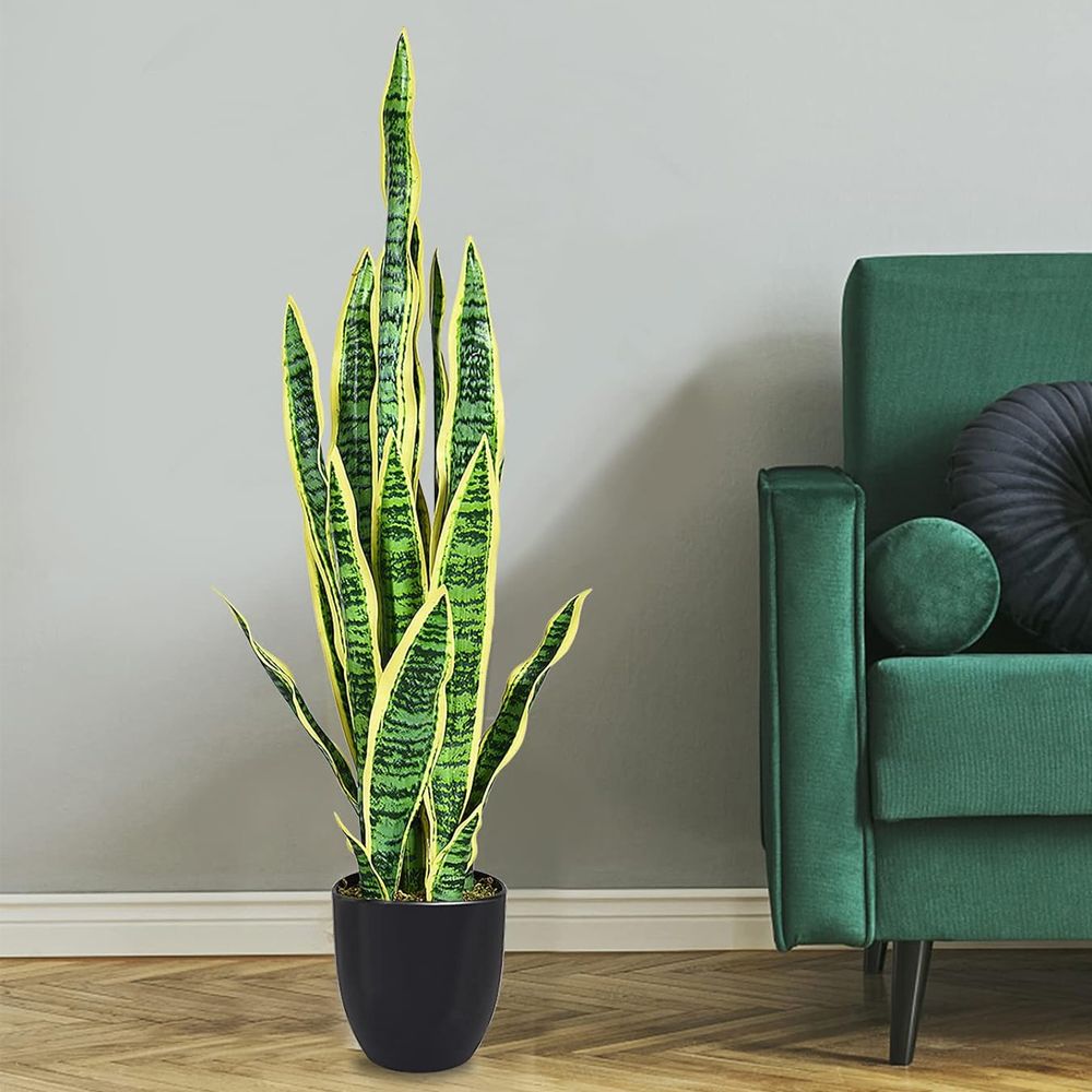 Tall artificial snake plant decor in a modern pot beside a green couch for stylish interior design