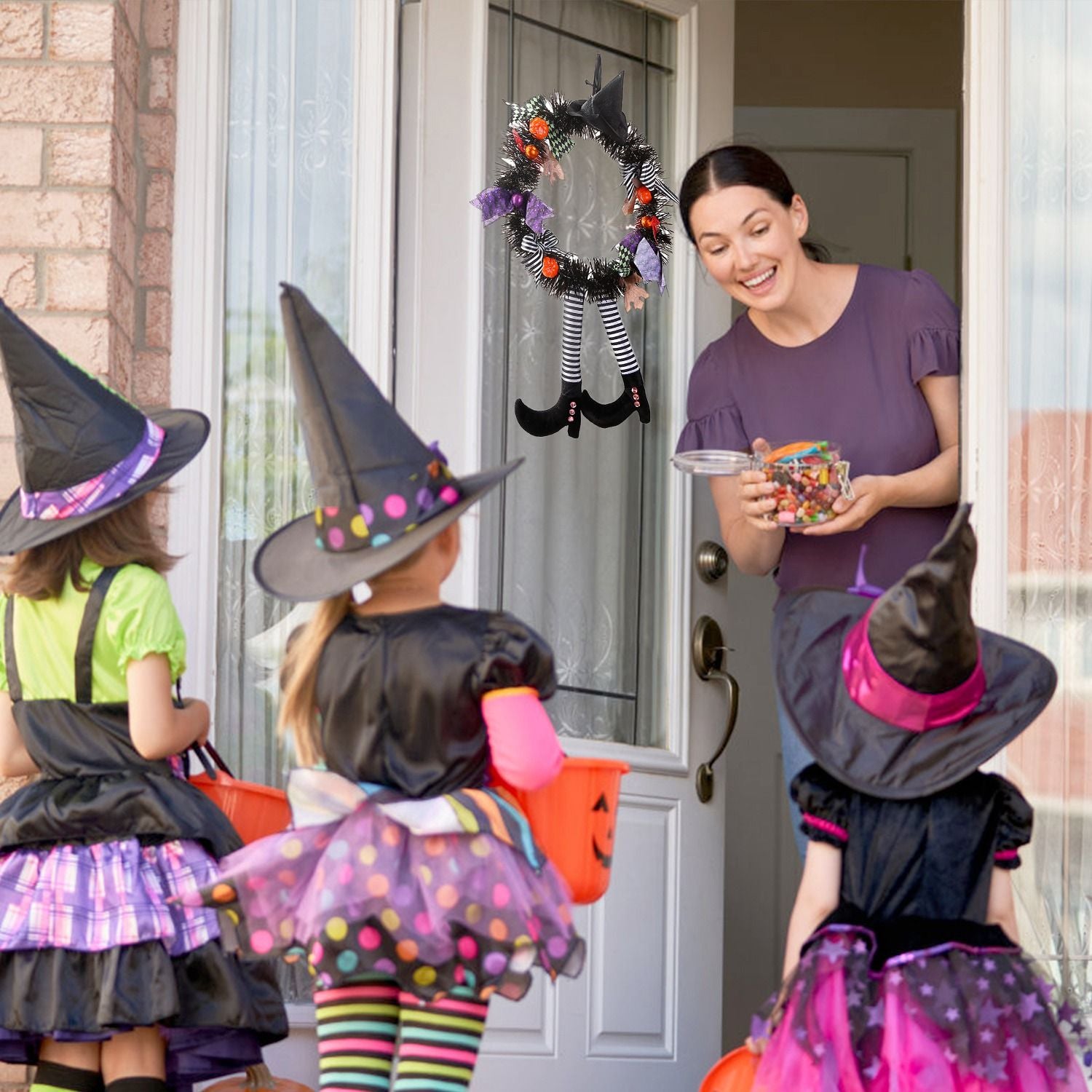 Halloween witch wreath hanging on front door with kids trick or treating in witch costumes