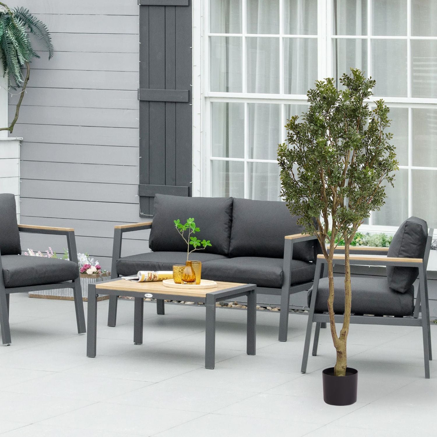 Large artificial plants in a stylish outdoor seating area featuring gray furniture and a wooden coffee table