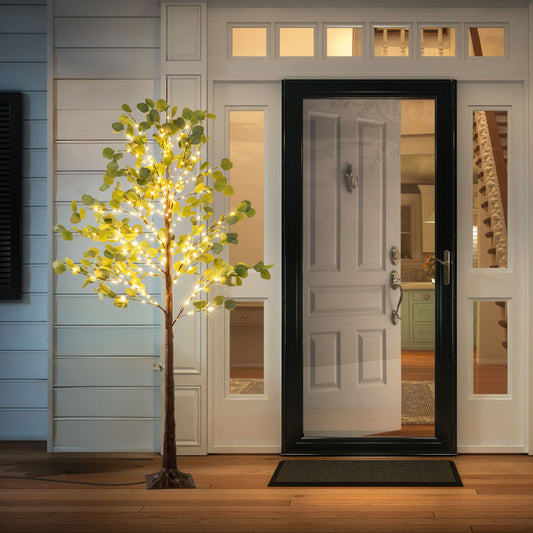 Lighted artificial olive tree with warm white lights by front door on porch at night