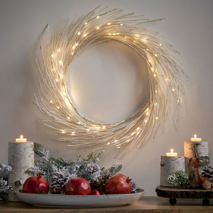 Lighted paper wreath with warm white lights hanging on wall above holiday table decor with candles and pine cones