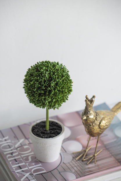 Mini faux topiary set in white pot placed on a book next to a gold decorative bird figurine