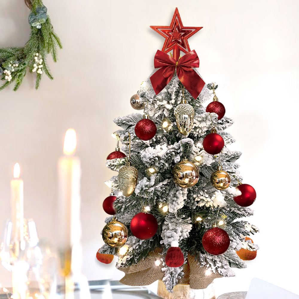 Mini tabletop Christmas tree with snow-covered branches decorated with red and gold ornaments and a red star topper