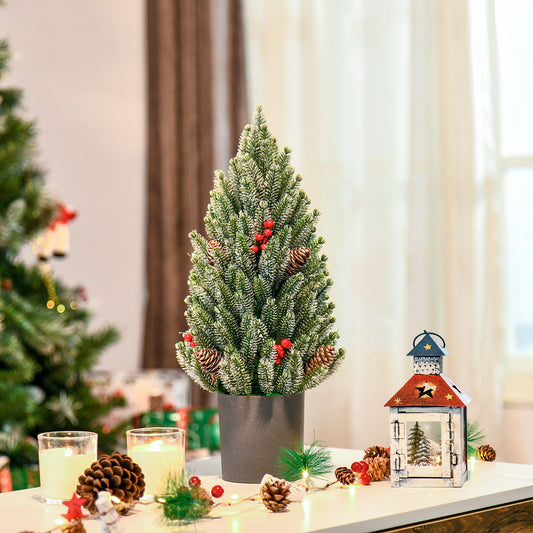 Miniature snow flocked Christmas tree with red berries and pinecones in a decorative pot