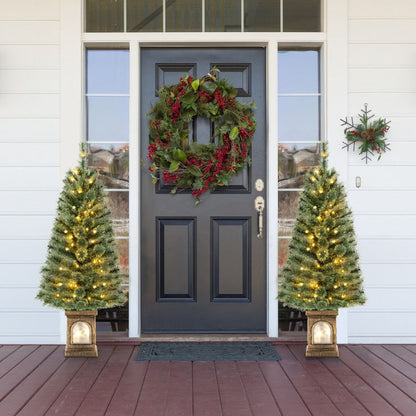 Two pre-lit artificial Christmas trees flanking a front door with holiday wreath and decorations