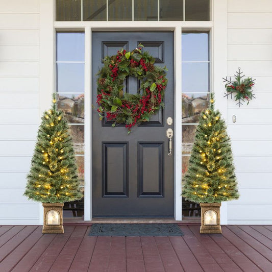 Two pre-lit artificial Christmas trees flanking a front door with holiday wreath and decorations