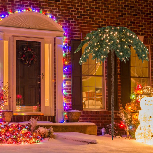 Pre-lit Christmas palm tree decorated with white lights in snowy front yard holiday display
