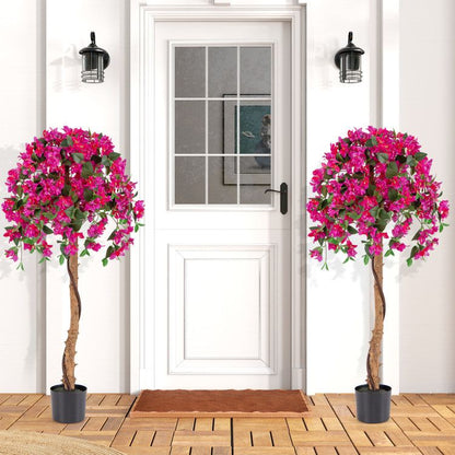 Artificial azalea tree set with vibrant pink flowers in black pots placed on wooden floor by white door