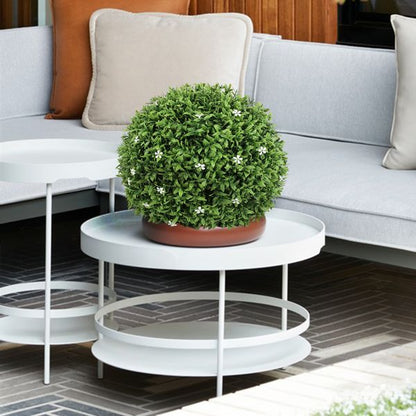 Artificial boxwood topiary ball with small white flowers on white round table in modern living room