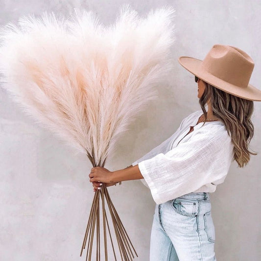 Woman holding tall artificial pampas grass decor with beige feathery plumes and long stems