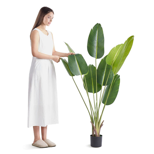 Woman in white dress standing next to artificial birds of paradise tree in black pot from FauxMart.com