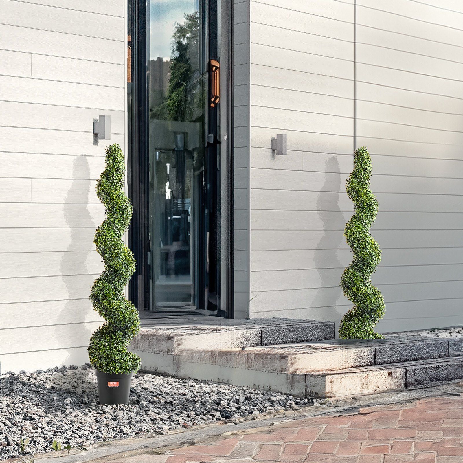 Artificial boxwood topiary tree set with spiral design in black pots placed outside modern home entrance