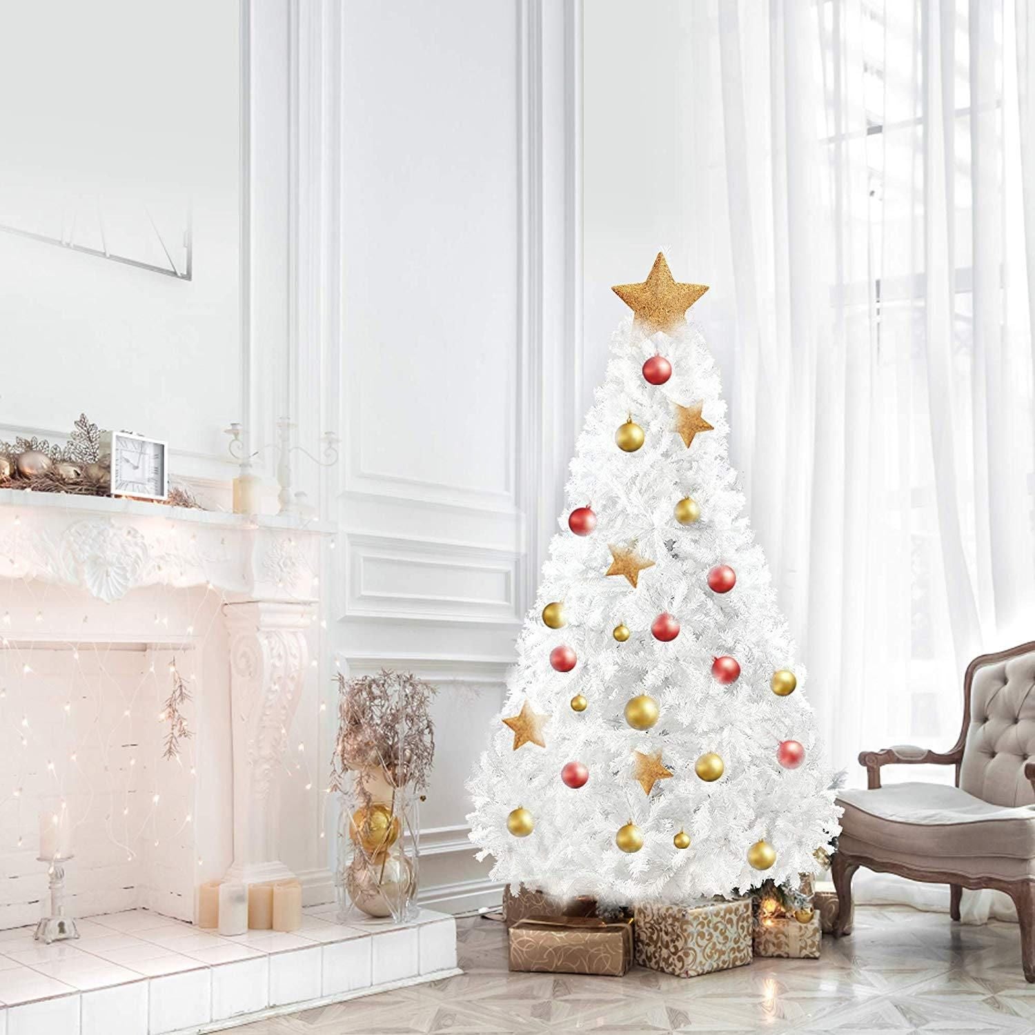 White artificial Christmas tree decorated with gold and red ornaments beside a fireplace in a bright living room